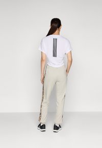 Hvit t-skjorte med sorte vertikale striper på baksiden, kombinert med beige bukser med leopardmønstret sidestriper og svarte joggesko.