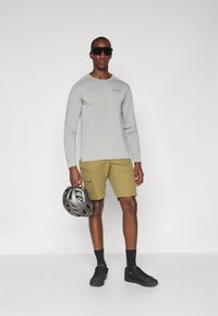Gray long-sleeve shirt, olive cargo shorts, black sneakers, and sunglasses; holding a gray bicycle helmet; minimal design, functional details.