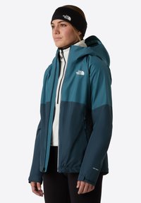 Teal and navy waterproof jacket with a fitted hood and zippered front. Features zippers, soft texture, and logo on the chest.