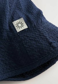 Cappello a secchiello blu navy realizzato in tessuto testurizzato, con un motivo cucito e una toppa quadrata con un disegno di sole sul lato.