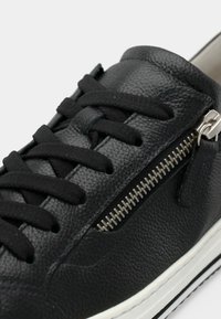 Μαύρο δερμάτινο αθλητικό παπούτσι με υλικό με υφή, μαύρα κορδόνια και πλευρικό φερμουάρ με ασημένιες λεπτομέρειες. Λευκή σόλα από καουτσούκ με μαύρες πινελιές.