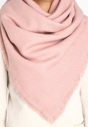 Écharpe rose pâle texturée avec un motif chevron subtil, drapée autour du cou sur un manteau beige clair.