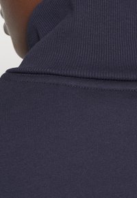 Tejido acanalado de color azul marino con un detalle de cuello alto, que muestra una superficie texturizada y costuras limpias a lo largo de los bordes.
