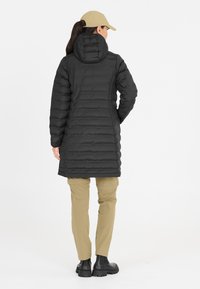 Sort quiltet puffer jakke med hætte, mellemlang stil. Parret med lyse beige bukser og sorte ankelstøvler. Enkel og funktionel stil.