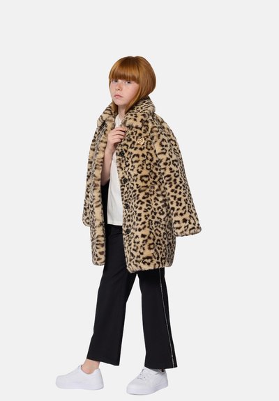 Leopard-print faux fur coat with a wide collar, button closures, and an accent pocket, worn over a white top and black trousers. White shoes.