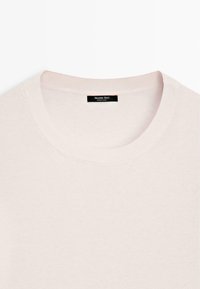 cremefarbener Strickpullover mit rundem Halsausschnitt und einem kleinen schwarzen Etikett innen im Kragen mit der Aufschrift "Massimo Dutti Made in China".