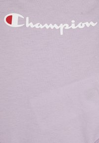 Lavendel Baumwoll-T-Shirt mit einem weißen geschwungenen "Champion"-Logo und einem roten Akzent im "C" für Branding-Details.