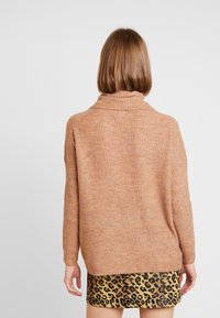 Loszittende trui met lange mouwen in zacht, lichtbruin materiaal met een gestructureerde textuur en een hoge kraag, gecombineerd met een rok met luipaardprint.