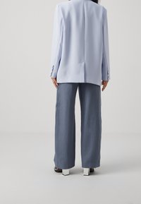 Světle modrý oblekový blejzr s dlouhými rukávy, s jedním rozventilovaným dílem na zadní straně, v kombinaci s volnými šedými kalhotami. Výrazné bílé boty na blokovém podpatku.