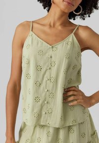 Ljusgrön ärmlös topp med V-ringning, blommiga broderade mönster och knappslå fram. Tillverkad av texturerad tyg.