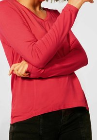 Růžové tričko s dlouhým rukávem, s kulatým výstřihem a měkkým, hladkým materiálem. Vrstvený design se zakřiveným lemem a přiléhavými rukávy.