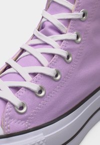 Κοντινό πλάνο μοβ καμβά αθλητικού παπουτσιού με λευκά κορδόνια περασμένα μέσα από μεταλλικά κρικάκια και λευκή ελαστική σόλα με μαύρο περίγραμμα.