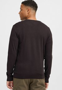 Pull en tricot marron foncé avec manches longues et col rond. Poignets et ourlet côtelés, avec une texture lisse et des détails de conception minimaux.