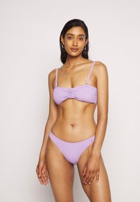 Biquíni roxo texturizado com um bralette ajustado apresentando um nó central e alças ajustáveis, combinado com cuecas de corte baixo a condizer.