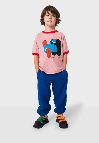 Camiseta de manga corta roja y rosa con un gráfico de un perro de dibujos animados colorido, combinada con pantalones de chándal azules y sandalias multicolores.