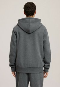 Szara bluza z kapturem z dużym kapturem, miękka w dotyku, z prążkowanym wykończeniem dołu i mankietów. Charakteryzuje się luźnym fasonem, pokazana od tyłu z pasującymi spodniami.