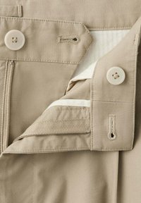 Ceinture de pantalon beige montrant une fermeture éclair, des boutons, des boutonnières et une doublure intérieure en tissu.