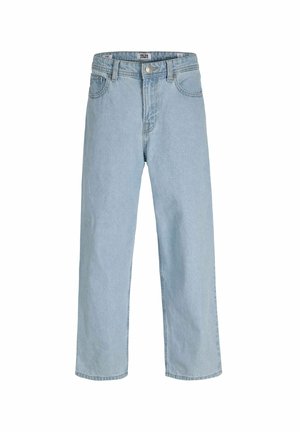 Un adolescent souriant portant un sweat à capuche bleu, un jean bleu clair et des baskets blanches devant un fond clair uni.