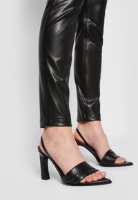 Svarta högklackade sandaler med öppen tå, med ett brett band över foten och en slät, glänsande läderfinish.