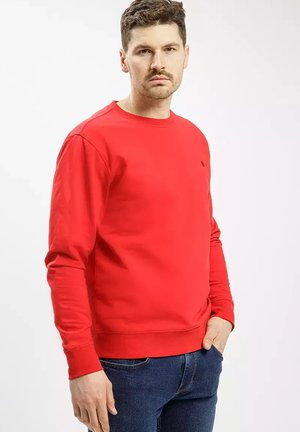 Czerwony sweter z okrągłym dekoltem, wykonany z mieszanki bawełny, z długimi rękawami i prążkowanymi mankietami, w zestawie z niebieskimi dżinsami. Obecny mały detal logo.