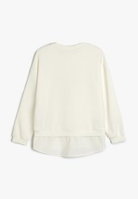 Sudadera de color crema claro con un cuello redondeado, mangas largas, puños de canalé y un dobladillo trasero ligeramente más largo. Tejido suave con una textura lisa.