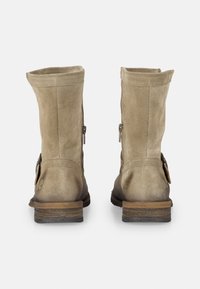 Stivali ankle in suede color tan con punta rotonda, cerniere laterali e dettagli decorativi in pelle marrone sul retro. Tacco piatto in legno sovrapposto.