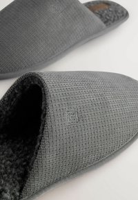 Graue Stoffschuhe mit strukturiertem Strickdesign, offenem Zehenbereich, weicher Innenauskleidung und dezentem Logodetail an der Seite.