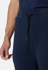Joggers azul marino con cintura elástica y cordón negro, bolsillos laterales y una superficie de tejido texturizado.