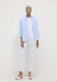 Helles blaues Hemd mit aufgerollten Ärmeln, kombiniert mit weißen Bundhose mit Kordelzug. Weiße Absatzschlappen und ein weißes Haarband runden den Look ab.