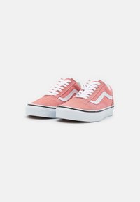 Różowe zamszowe sneakersy typu low-top z białymi sznurówkami i akcentami w formie logo, z białą gumową podeszwą i czarnym wykończeniem przy podstawie.