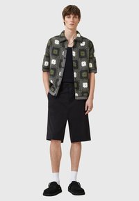 Cămașă scurtă cu mâneci verzi și gri, cu modele florale, pantaloni scurți negri, șosete albe și pantofi slip-on negri. Design simplu, croială lejeră.