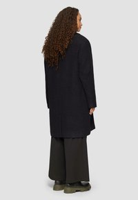 Dunkelblauer Fischgrätenmantel aus strukturiertem Stoff, mit leicht oversized Passform, langen Ärmeln und geradem Schnitt.