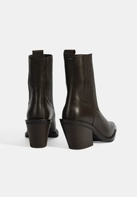 Bottes de cheville en cuir brun et brillant avec des coutures verticales et un bout rectangulaire, présentant un design à talon épais et une languette.