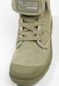 Sneakers w kolorze oliwkowym z płótna, z gumową podeszwą, okrągłym noskiem, metalowymi oczkami i sznurowanym zapięciem. Posiadają wyściełany kostkę oraz metkę z logo.