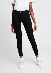 Jeans ajustados negros con una cintura alta y cremalleras laterales en los tobillos. Hechos de denim elástico para un silueta ceñida.