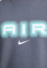 Gray cotton t-shirt featuring the word "AIR" in blue with layered lines, along with a small white Nike swoosh logo at the bottom.