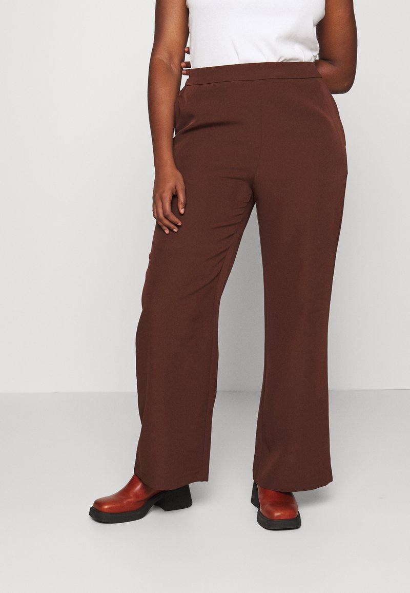 Pantalon marron à jambes larges en tissu lisse, avec une taille haute et des poches latérales, associé à des bottines rouges.