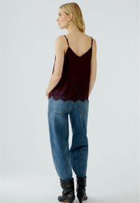 Bordeauxfarbener Tanktop mit Spitzenbesatz, verstellbaren Trägern, kombiniert mit lockeren blauen Jeans und schwarzen Knöchelstiefeln. Schlichte und entspannte Silhouette.