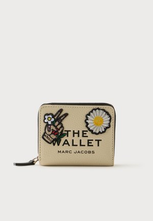 Portefeuille beige à fermeture éclair avec logo Marc Jacobs, patchs main faisant le signe de paix et marguerite, et texte « THE WALLET » sur le devant.