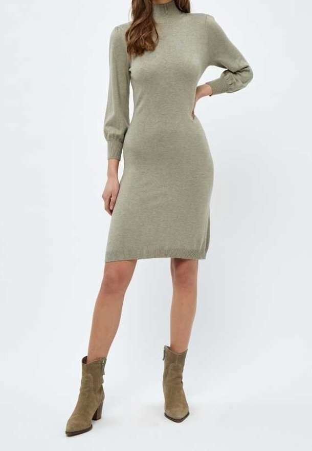 Femme portant une robe en tricot marron clair, à manches longues, longueur genou, avec un col montant, et des bottines marron assorties.