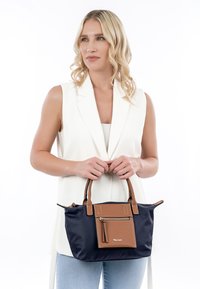 Borsa a mano blu navy con dettagli in pelle marrone, dotata di una tasca frontale con zip, manici doppi e una superficie in tessuto liscio.