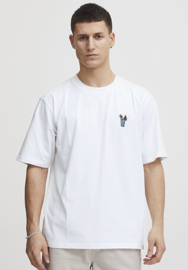 Hvit bomulls t-skjorte med korte ermer, med et lite, fargerikt brodert design på brystet. Klassisk rund hals og avslappet passform.