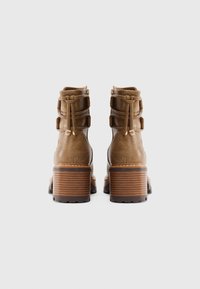 Braune Leder-Ankle-Boots mit strukturiertem Finish, ausgestattet mit einem gestapelten Absatz und dekorativen Rückengurten. Seitlicher Reißverschluss für ein einfaches An- und Ausziehen.