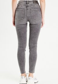 Hoge taille, nauwsluitende grijze jeans met een lichte textuur, vijf zakken en een rafelige zoom bij de enkel.