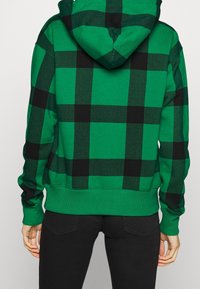 Zelená kostkovaná mikina s kapucí a černým vzorem. Obsahuje kapuci a žebrované manžety, vyrobená z texturované tkaniny. Viditelné černé akcenty.