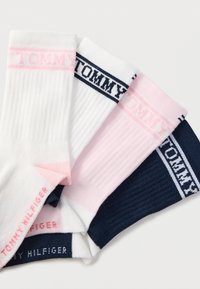 Τέσσερα ζευγάρια ριγωτές κάλτσες μέσης σε λευκό, ροζ και ναυτικό μπλε, κάθε μία με λωρίδες με το λογότυπο "Tommy" και το κείμενο "Tommy Hilfiger" στο πέλμα.