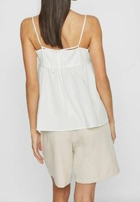 Vit ärmlös topp med tunna axelband och en knytning i ryggen, i kombination med ljusbeige shorts som har en loose, flödande design.