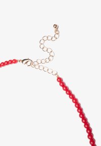 Collar de cuentas rojas con cuentas redondas brillantes, que cuenta con un cierre de metal en tono dorado y una cadena ajustable para personalizar la longitud.