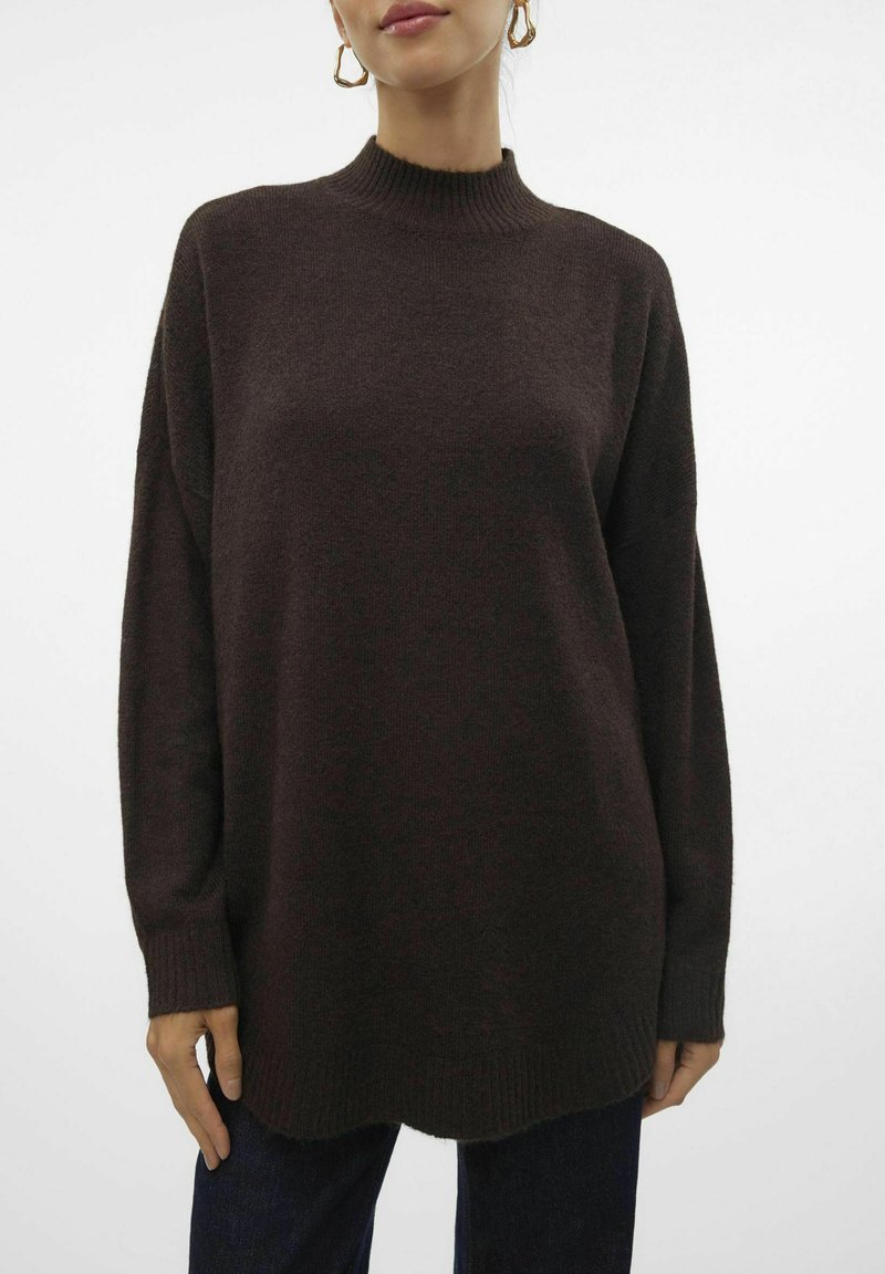 Pull en maille texturée, surdimensionné, marron foncé avec un col montant, des épaules tombantes et des poignets côtelés. Se termine par une légère courbe à l'ourlet.