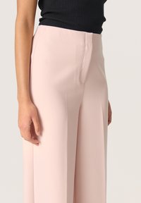 Bleg pink højtaljede bukser i et glat, blødt stof. Har et lige ben-design med en matchende syning og en forkant.